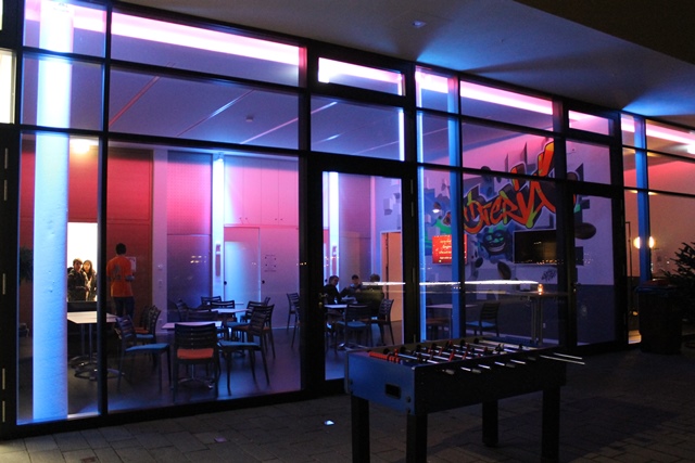beleuchteter Jugendpavillon mit Tischkicker im Freien und Sitzgruppen im Inneren.