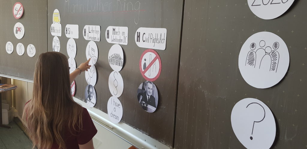 SchÃ¼lerin prÃ¤sentiert an der Tafel Martin Luther King und zeigt auf ein rundes Symbolbild